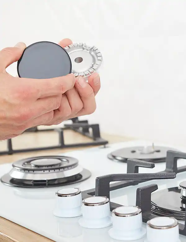A person holding parts of a gas stove burner, with a gas stove in the background.
