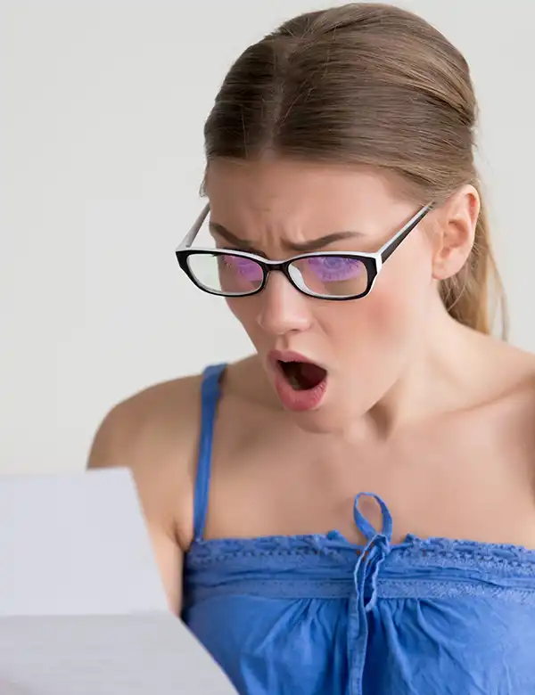 A woman with glasses and a blue top looks surprised while reading a water bill with an unexplained increase.
