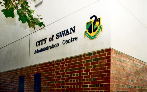 A building corner showing a sign that reads "CITY of SWAN Administration Centre" and an adjacent emblem on a white wall above a brick base section.