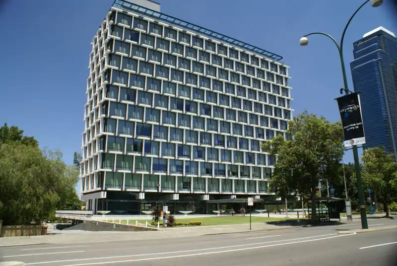 A multi-story office building with a modern grid-like facade, situated along a city street with trees and a lamp post visible in the foreground.